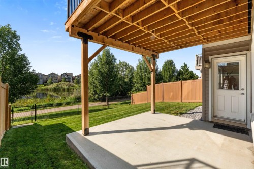 Covered concrete patio with a wood-finished ceiling, expansive green lawn, and a fenced perimeter - 3334 Parker Loop Sw, Edmonton, AB 